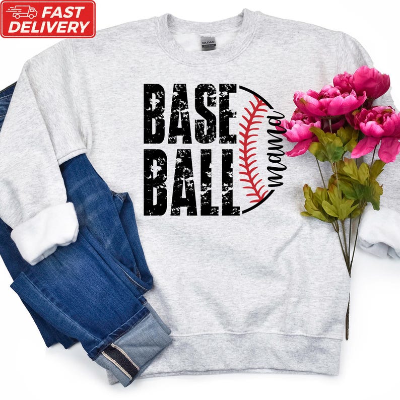 A gray sweatshirt with the text "BASE BALL" printed on it, along with a baseball graphic and the word "Momma" below it. The sweatshirt is placed next to a pair of blue jeans and a bouquet of pink flowers.