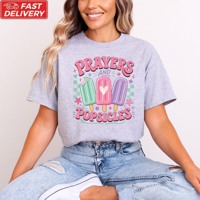 A woman wearing a gray t-shirt with a graphic design of three popsicles and the text "Prayers and Popsicles" printed on it.