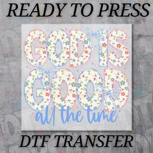 May include: A DTF transfer with the words "GOD IS GOOD all the time" in a floral pattern with blue bows. The words "READY TO PRESS" and "DTF TRANSFER" are above and below the main text.