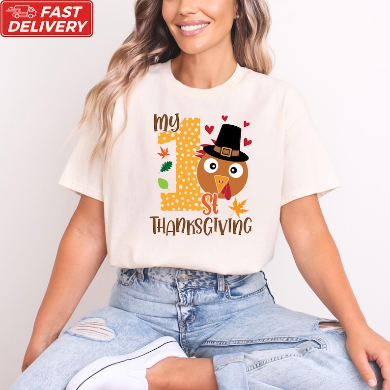 A woman wearing a white t-shirt with a graphic design of a turkey wearing a Thanksgiving hat and the text "My 1st Thanksgiving" printed on it.