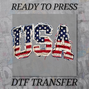 May include: A gray background features the word "USA" in a patriotic design. The letters are crafted with a denim-like texture, adorned with the American flag's stars and stripes, and trimmed with lace. The text "READY TO PRESS" and "DTF TRANSFER" are above and below the main design.