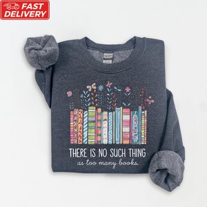 A gray sweatshirt with a colorful graphic design depicting a row of books and flowers, along with the text "THERE IS NO SUCH THING as too many books" printed on it.