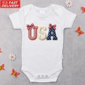 A white baby onesie with the word "USA" embroidered on it, surrounded by decorative elements such as flowers and butterflies.