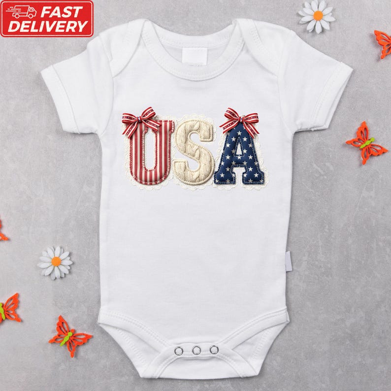 A white baby onesie with the word "USA" embroidered on it, surrounded by decorative elements such as flowers and butterflies.
