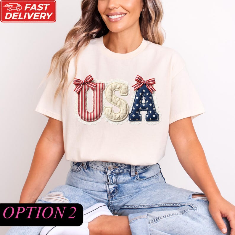A woman wearing a white t-shirt with the word "USA" embroidered on it, sitting on the ground.