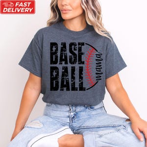A woman wearing a gray t-shirt with the text "BASE BALL" printed on it, sitting on the ground.