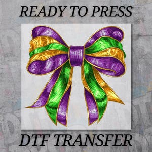 May include: A colorful bow design with purple, green, and gold ribbons. The image includes the text "READY TO PRESS" at the top and "DTF TRANSFER" at the bottom. The bow is centered on a white background.