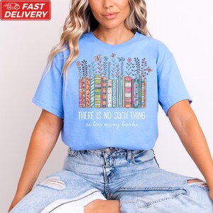 A woman wearing a blue t-shirt with a colorful graphic design of books and flowers, along with the text "THERE IS NO SUCH THING as too many books" printed on it.