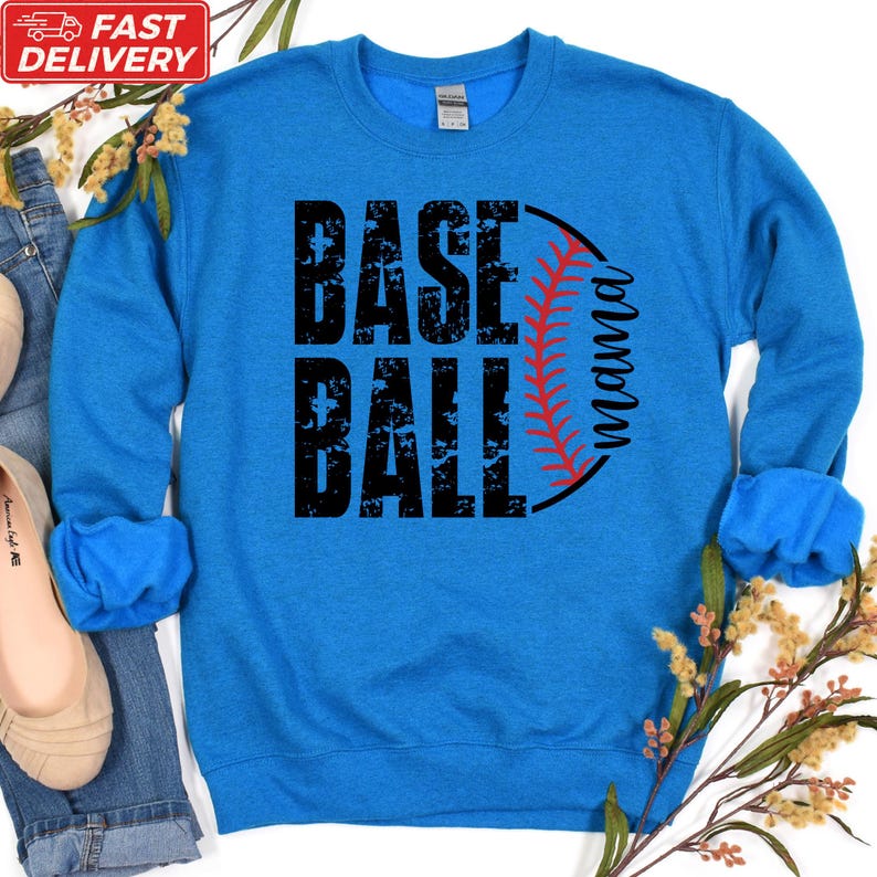 A blue sweatshirt with the text "BASE BALL" printed on it, along with a baseball graphic. The sweatshirt is placed on a white background, and there are some flowers and a pair of shoes visible in the image.