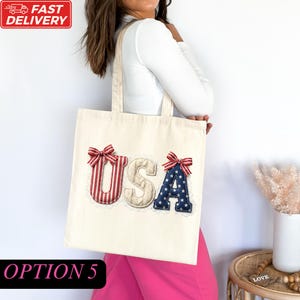A woman wearing a white shirt and pink pants is holding a tote bag with the word "USA" printed on it.