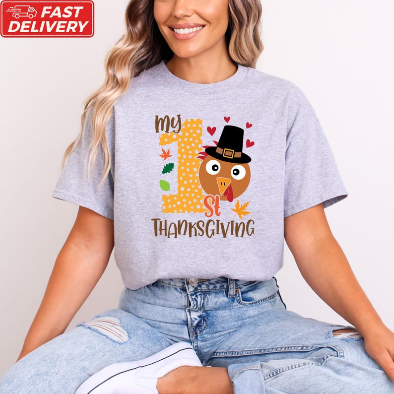 A woman wearing a gray t-shirt with a graphic design of a turkey wearing a hat and the text "My 1st Thanksgiving" printed on it.