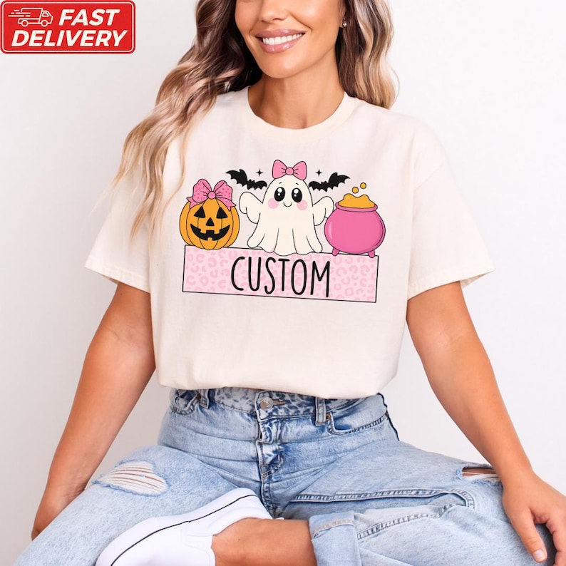A woman wearing a white t-shirt with a Halloween-themed graphic design, including a ghost, pumpkin, and a pink pot.