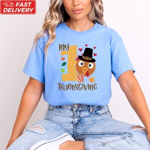 A woman wearing a blue t-shirt with a turkey graphic and text that says "My 1st Thanksgiving".