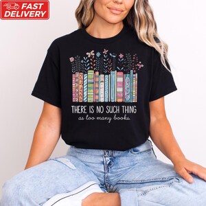 A woman wearing a black t-shirt with a colorful graphic design of books and the text "THERE IS NOSuch THING as too many books" printed on it.