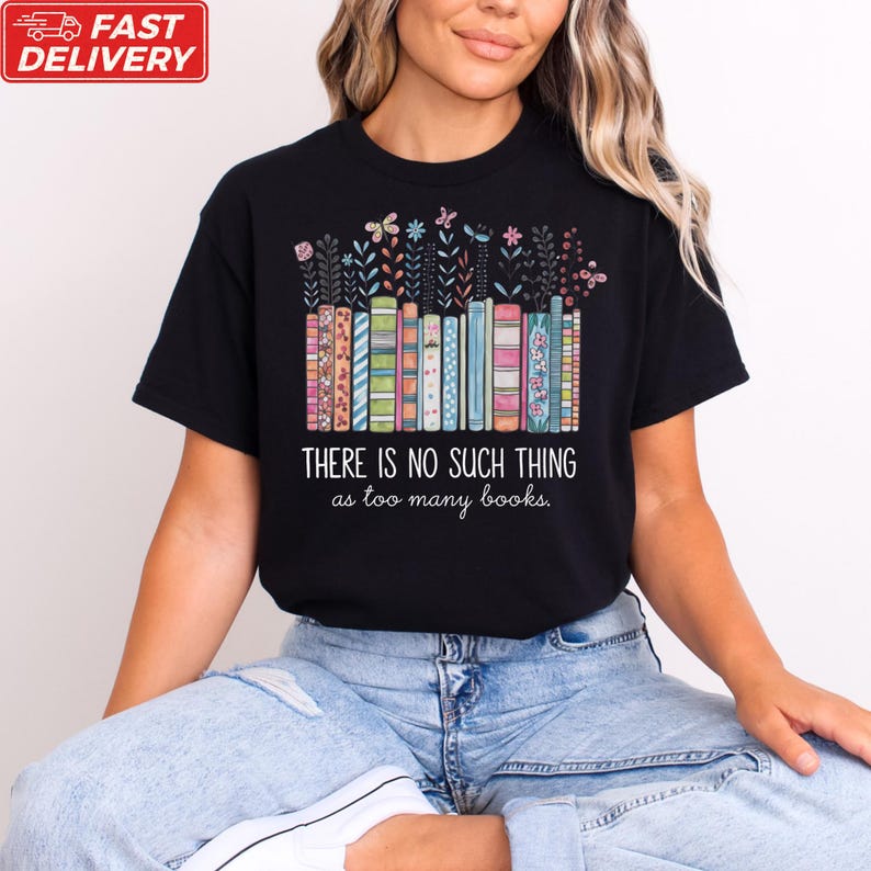 A woman wearing a black t-shirt with a colorful graphic design of books and the text "THERE IS NOSuch THING as too many books" printed on it.
