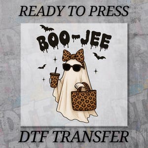 May include: A DTF transfer featuring a cartoon ghost wearing sunglasses and a bow, holding a drink and a leopard print bag. The text "BOO-JEE" is above the ghost, with "READY TO PRESS" and "DTF TRANSFER" at the top and bottom.