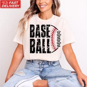 A woman wearing a white t-shirt with the text "BASE BALL" printed on it, sitting on the ground.