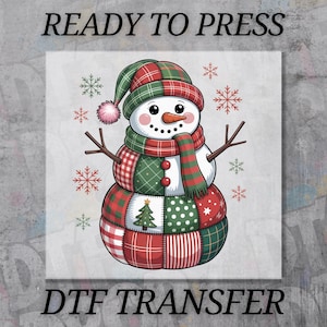 May include: A whimsical snowman design with a patchwork pattern in red, green, and white. The snowman wears a matching hat and scarf, with twig arms and a carrot nose. The text "READY TO PRESS" and "DTF TRANSFER" are displayed.