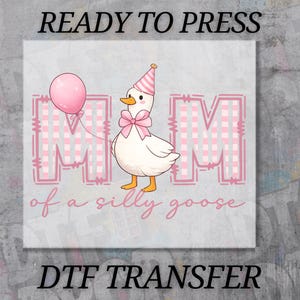 May include: A DTF transfer featuring a white goose wearing a pink and white striped party hat and a pink bow. The goose holds a pink balloon. Behind the goose are two large letters M with a pink and white gingham pattern. Text reads: MOM of a silly goose.