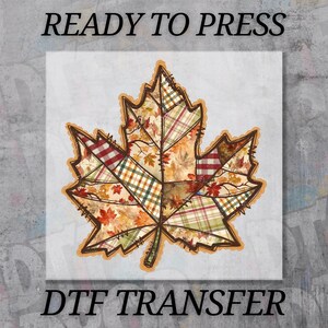 May include: A fall-themed DTF transfer featuring a patchwork maple leaf design. The leaf is composed of various plaid and leaf patterns in shades of orange, red, and green, with a decorative border. The text "READY TO PRESS" and "DTF TRANSFER" are displayed.