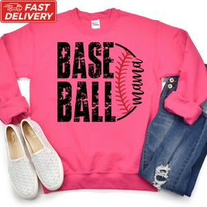 A pink sweatshirt with the text "BASE BALL" printed on it, along with a baseball graphic, is displayed alongside a pair of white sneakers and a pair of blue jeans.