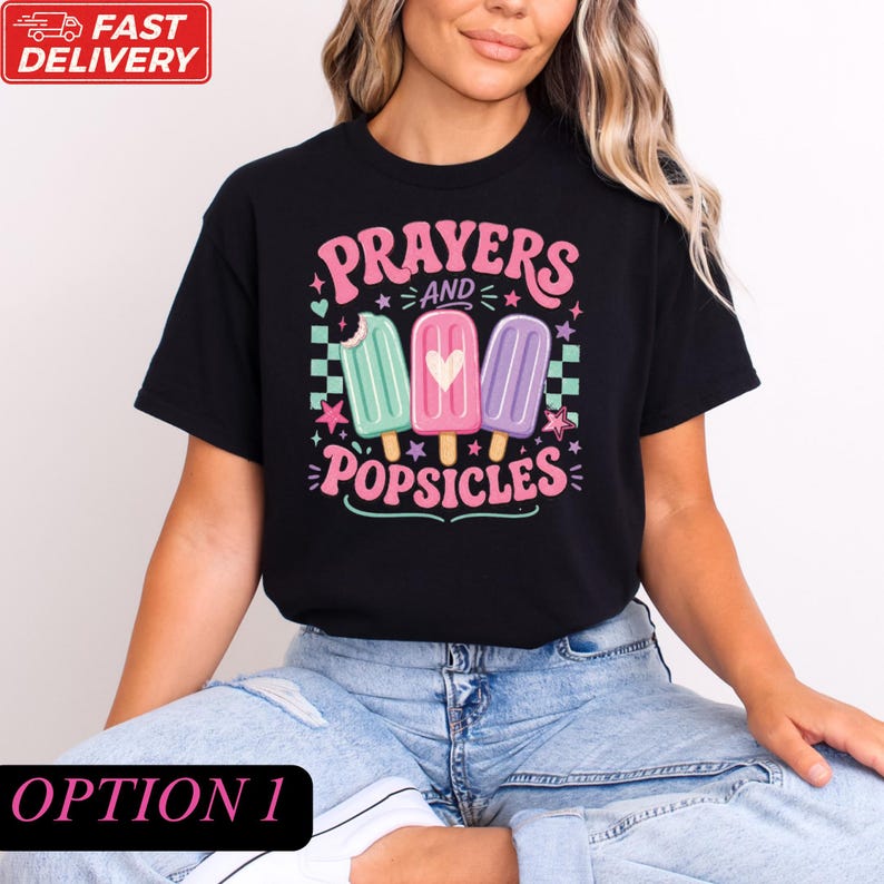 A woman wearing a black t-shirt with a colorful graphic design featuring three popsicles and the text "Prayers and Popsicles".