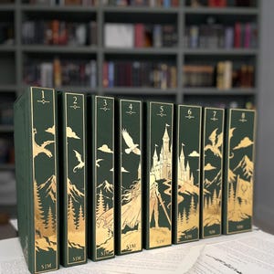 May include: A set of eight dark green books arranged in a row, each featuring gold foil illustrations on the spine. The spines display sequential numbers from one to eight, along with gold imagery of mountains, forests, castles, and dragons.