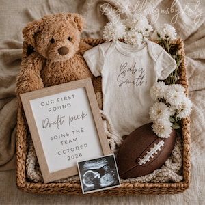 Puede incluir: Una cesta tejida que contiene un oso de peluche marrón, un body de bebé acanalado de color crema con el texto Baby Smith, un marco de madera con el texto OUR FIRST ROUND Draft pick JOINS THE TEAM OCTOBER 2026, un balón de fútbol y flores blancas.