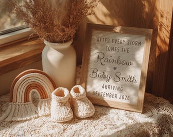 Pode incluir: Uma cena de berçário em tons neutros com um anúncio emoldurado que diz "After every storm comes the Rainbow Baby Smith arriving September 2026." Inclui um arco-íris de macramé, um par de botinhas de bebê de crochê e um vaso com flores secas.