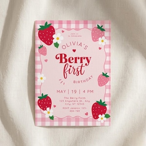 May include: A pink and white gingham-patterned invitation card with the text "Olivia's Berry First Birthday." The card features illustrations of strawberries, white flowers, and hearts. The date and time of the event are also included.