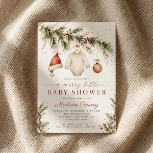 May include: A rectangular invitation card featuring a watercolor illustration of pine branches with red berries, a red Santa hat, a cream-colored baby onesie, and a red ornament. The text reads: Please join us for a merry little baby shower.