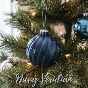 May include: Navy blue glass Christmas ornament with a swirled design, hanging on a decorated evergreen tree. The text "Navy Veridian" is displayed on the image. Other ornaments are visible.