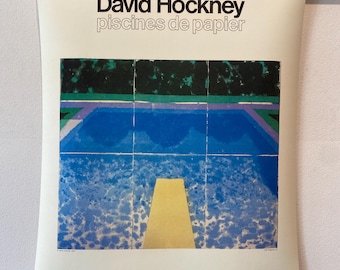 May include: A poster titled "David Hockney piscines de papier" featuring a colorful depiction of a swimming pool with a diving board. The poster is held in place by black binder clips and a wooden rod.