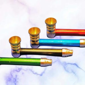 May include: Four colorful metal pipes with gold-colored bowls and mouthpieces. The pipes are in red, blue, gold, and green. The background is a light blue and white marbled pattern.