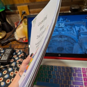 Peut inclure: Une pile de feuilles de papier blanc reli&eacute;es ensemble, avec le texte imprim&eacute; "Growing into 2nd Grade" sur la couverture. Le document comprend des &eacute;l&eacute;ments graphiques color&eacute;s et est tenu verticalement, montrant la tranche du papier.