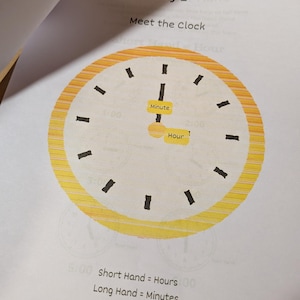 May include: A printed educational worksheet titled Day 1 Meet the Clock featuring a yellow striped circular clock face with black hour markers. The clock has two hands labeled with yellow rectangular tags reading Minute and Hour. Text below reads Short Hand = Hours and Long Hand = Minutes.