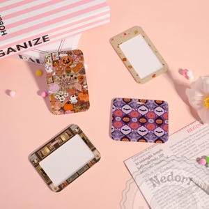 May include: Four rectangular Halloween-themed ID badge holders. One features a collage of pumpkins, ghosts, and other festive elements. Another has a pattern of bats and jack-o'-lanterns. The other two have a white center.