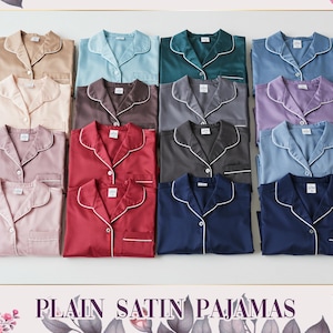 Può includere: Una collezione di pigiami in raso in vari colori, tra cui beige, blu, verde, grigio e bordeaux. Ogni top del pigiama ha un bordo bianco e una tasca sul petto. Il testo "PLAIN SATIN PAJAMAS" è visibile in basso.