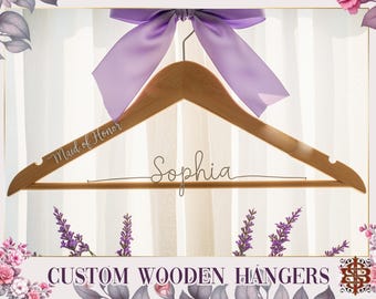 Könnte beinhalten: Ein Holzkleiderbügel mit den Schriftzügen "Maid of Honor" und "Sophia" in Schreibschrift. Er hat eine lila Schleife. Der Text "Custom Wooden Hangers" ist am unteren Bildrand zu sehen.