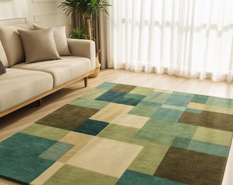 May include: A rectangular area rug with a geometric pattern in shades of green, blue, and beige. The rug is placed on a hardwood floor in a living room setting, with a beige sofa and a plant visible in the background.