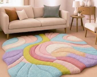 May include: A colorful, abstract area rug with a soft, textured surface. The rug features a flowing design in pastel shades of blue, pink, yellow, and purple. The rug is placed on a light-colored wooden floor in a living room setting.