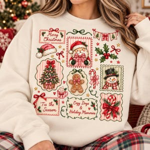 Puede incluir: Una sudadera de cuello redondo color crema con un estampado gráfico festivo que incluye varias ilustraciones navideñas como Santa Claus, un muñeco de nieve, un hombre de jengibre, un árbol decorado y bastones de caramelo.