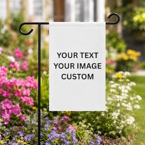 Puede incluir: Una bandera de jardín rectangular blanca colgada de un soporte de metal negro. La bandera presenta el texto impreso en negro: YOUR TEXT, YOUR IMAGE, CUSTOM. El diseño se muestra sobre un fondo de jardín desenfocado con flores coloridas.