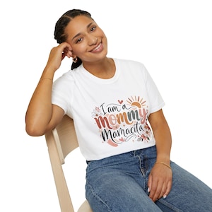 Puede incluir: Camiseta blanca con el texto "I am a mommy Mamacita" en un diseño floral colorido. El diseño incluye un sol, corazones y flores. La camiseta la lleva una persona con vaqueros azules.