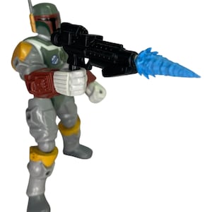 May include: A Boba Fett action figure from Star Wars, in a dynamic pose. The figure wears a gray and green suit with red and yellow details, holding a black blaster with a blue energy blast. A collectible toy.