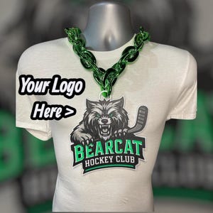 May include: White t-shirt with a green chain necklace and a Bearcat Hockey Club logo. The logo features a snarling wolf with a hockey stick. The text "Your Logo Here >" is printed on the shirt.