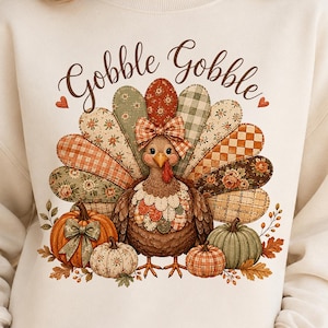 May include: A cream-colored crewneck sweatshirt featuring a graphic of a turkey with a patchwork-style tail in shades of orange, green, and brown. The turkey wears a plaid bow and is surrounded by pumpkins. The text Gobble Gobble is printed above.