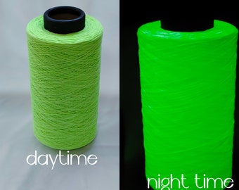 May include: A spool of bright green glow-in-the-dark yarn. The yarn is shown in both daylight and nighttime conditions. The yarn glows brightly in the dark.