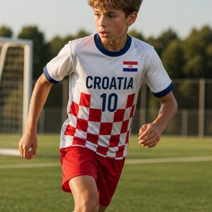 May include: A white football shirt with the word "CROATIA" and the number "10" printed on the front. The shirt has a red and white chequered pattern on the lower half. The shorts are red. The Croatian flag is on the right sleeve.