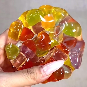 May include: A colourful, translucent slime toy with various shapes and sizes. The slime is a mix of yellow, orange, red, green, and purple, creating a vibrant and playful appearance. The toy is held in a hand, showcasing its texture and colour.